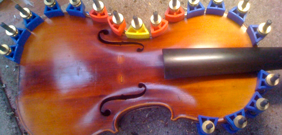 After repairing cracks in the top of the violin, and the glue has set, we’re in the process of removing clamp.